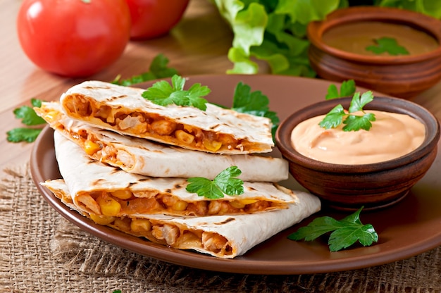 Mexican Quesadilla sliced with vegetables and sauces on the table