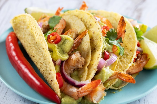 Mexican tacos with shrimpguacamole and vegetables on wooden table