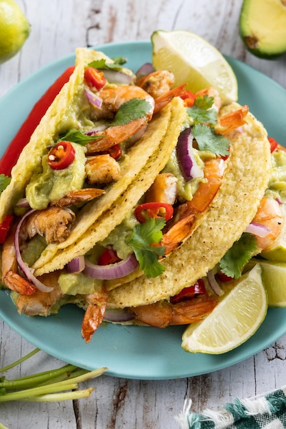 Mexican tacos with shrimpguacamole and vegetables on wooden table