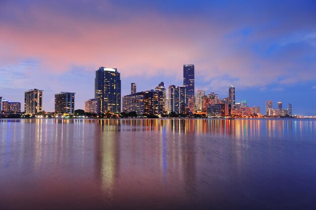 反射のある海の上の都市の高層ビルと夕暮れ時のマイアミ市のスカイラインのパノラマ