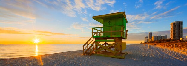 Miami South Beach sunrise with lifeguard tower and coastline with colorful cloud and blue sky.