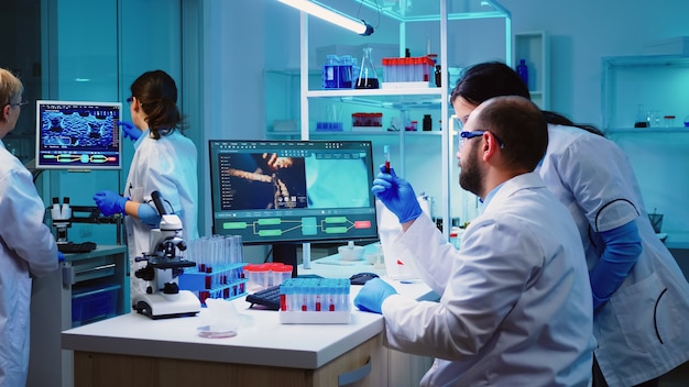 Microbiologist doctor taking a blood sample tube from rack with machines of analysis in the lab background