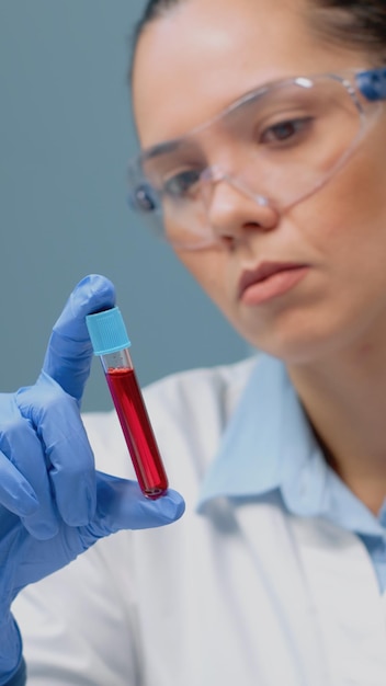Бесплатное фото Врач-микробиолог изучает vacutainer с жидкой кровью в медицинской лаборатории. ученый в перчатках и очках держит прозрачную трубку с красным раствором для фармацевтических разработок