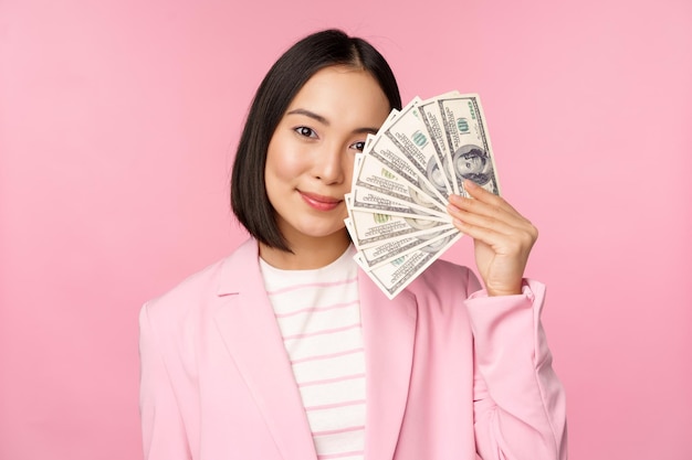 Microcredit investment and business people concept Young asian businesswoman corporate lady showing money cash dollars smiling pleased pink background