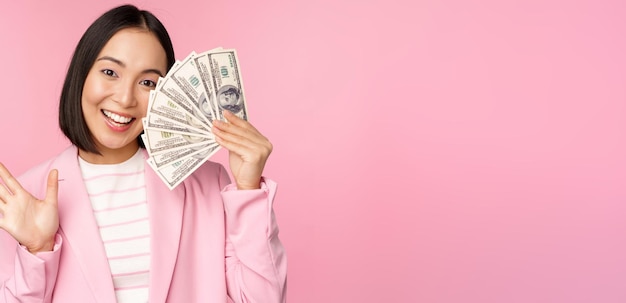 Free photo microcredit investment and business people concept young asian businesswoman corporate lady showing money cash dollars waving hand pink background