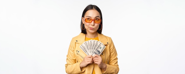 Microcredit and money concept Stylish asian young woman in sunglasses laughing happy holding dollars cash standing over white background