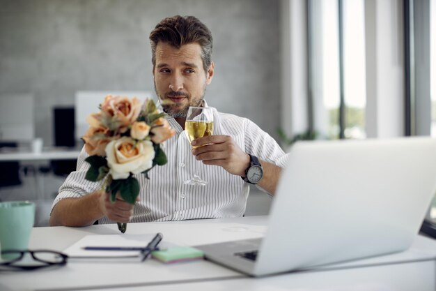 Бизнесмен среднего возраста пьет вино во время онлайн-свидания за ноутбуком