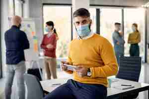 Free photo mid adult businessman working on touchpad and wearing protective face mask in the office