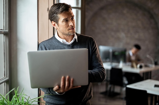 Free photo mid adult entrepreneur thinking of something while using computer by the window in the office