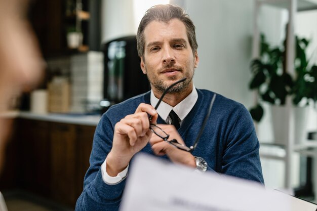 Mid adult insurance agent thinking of something while having consultations with his client