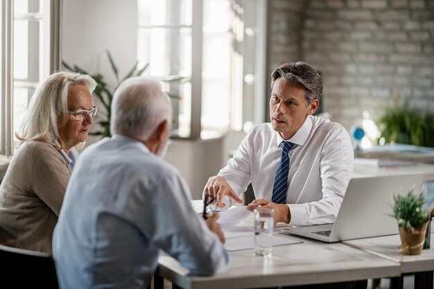 Mid adult insurance agent with mature couple analyzing financial reports and communicating during the meeting in the office