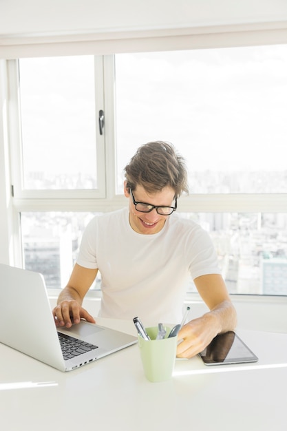 Середина взрослого человека в очках, используя ноутбук перед стеклянным окном