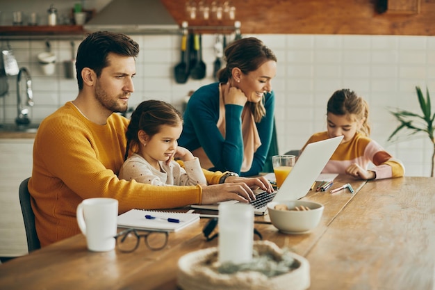 Metà uomo adulto che lavora al computer portatile mentre è con la sua famiglia a casa