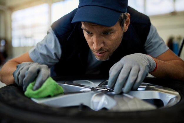 中年の整備士がワークショップで布で修理された車のタイヤを掃除する