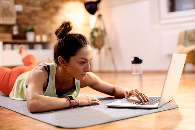 Mid adult sportswoman using computer while practicing on the floor at home