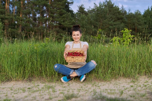 Женщина среднего возраста с корзиной свежей клубники в сельской местности, здоровой органической пищей