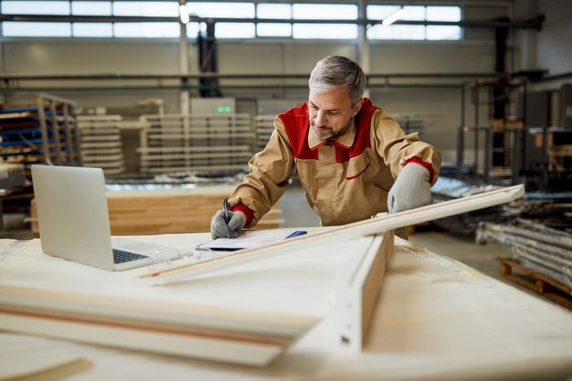 Mid adult worker taking notes while checking measurements at carpentry workshop