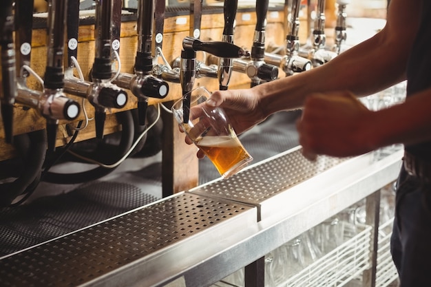 Free photo mid section of bar tender filling beer from bar pump