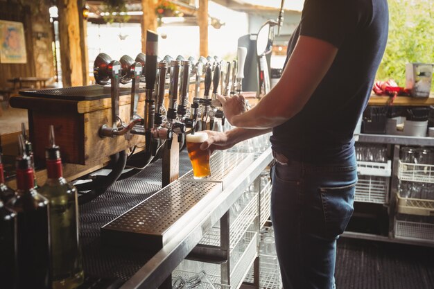 Mid section of bar tender filling beer from bar pump