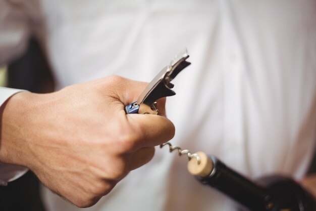 Mid section of bar tender opening a bottle of wine