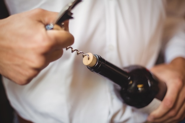 Mid section of bar tender opening a bottle of wine