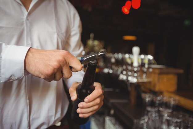 Mid section of bartender opening a beer bottle