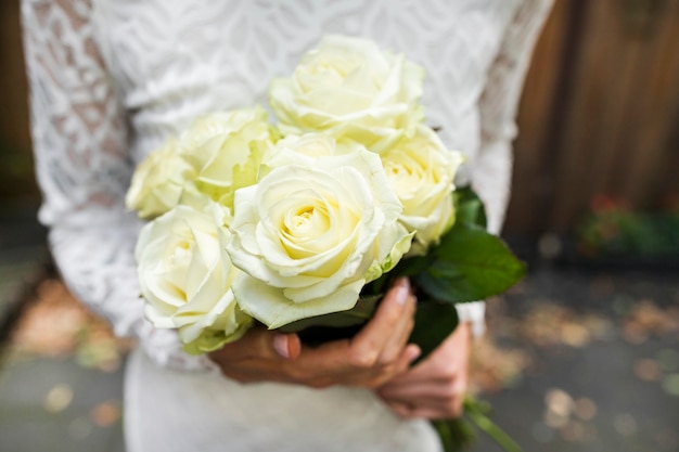 Mid section of bride holding bouquet of roses in hands