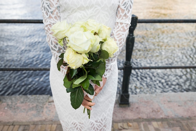 Mid section of bride holding bunch of roses in hands
