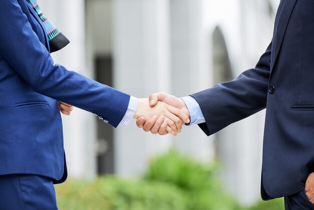 Mid-section of business people shaking hands outdoors