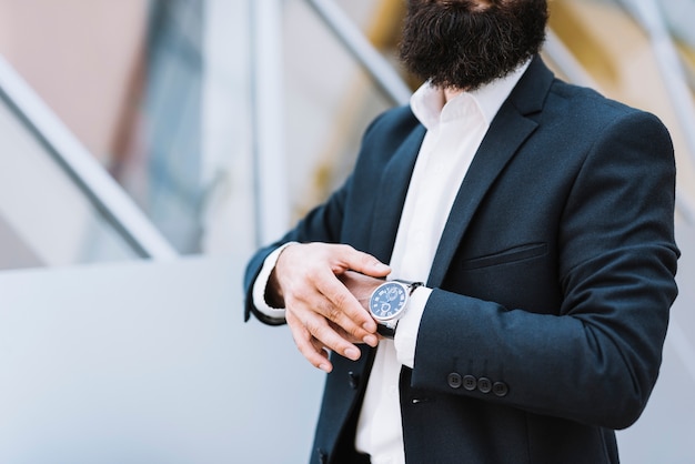 Foto gratuita metà di sezione dell'uomo d'affari che tiene orologio da polso sulla sua mano