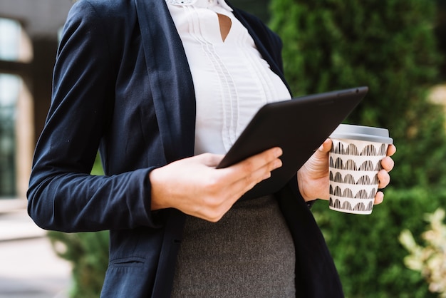 Mid section of businesswoman holding digital tablet and disposable coffee cup
