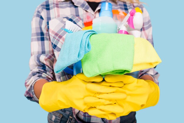 Mid section of cleaner holding bucket with cleaning products wearing yellow gloves