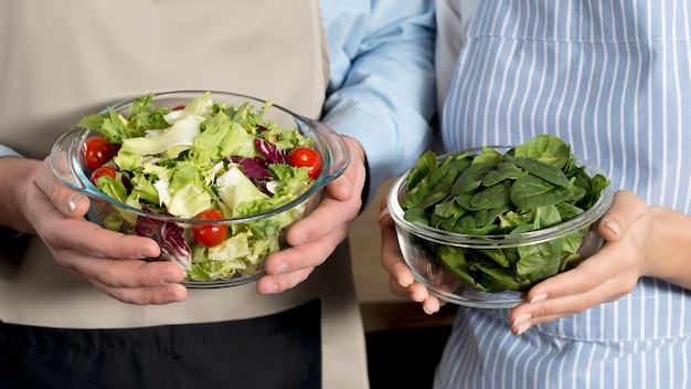 Mid-section of couple holding bowl of healthy salad and basil leafs