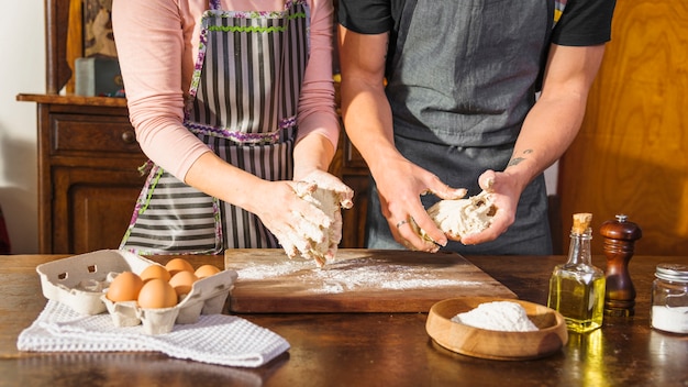 Foto gratuita metà di sezione delle coppie che preparano pasta con gli ingredienti di cottura sulla tavola di legno