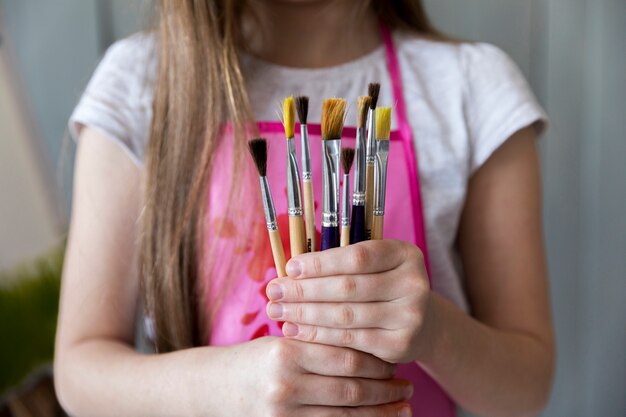 Mid section of a girl holding many paintbrushes in hand