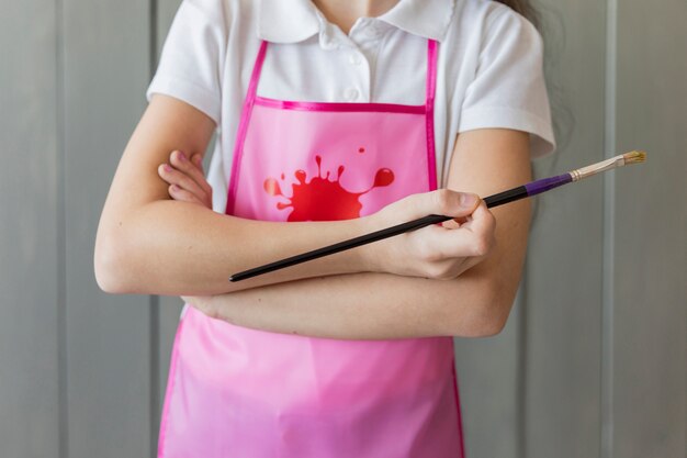 Mid section of a girl holding standing with arm crossed holding paintbrush in hand