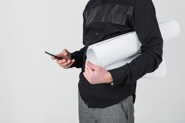 Mid section of a male architect holding blueprint using cellphone