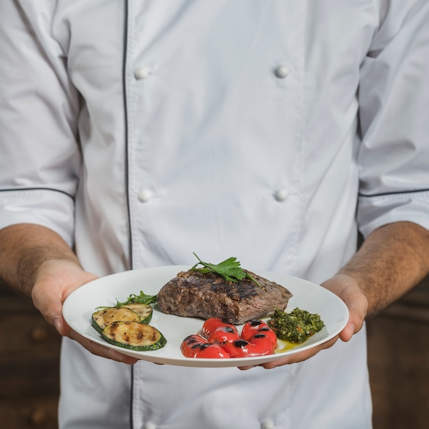 Mid section of male chef holding prepared beef steak with vegetables