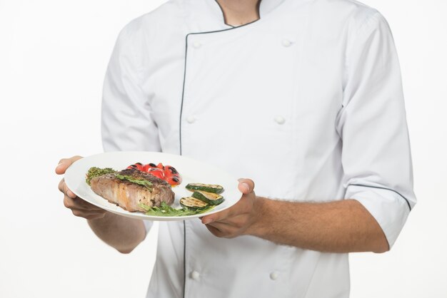 Mid section of male chef holding prepared dish with roasted beef steak and vegetables