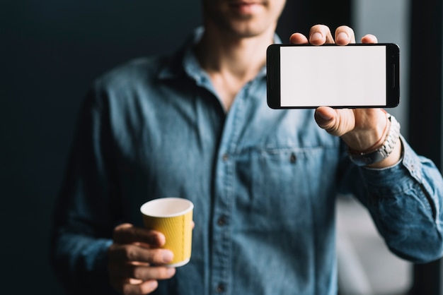 Metà di sezione di un uomo che tiene la tazza di caffè eliminabile che mostra lo schermo del cellulare