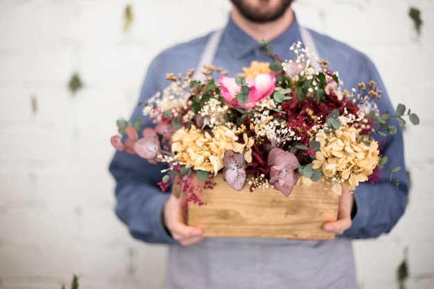 Free photo mid section of man holding wooden crate with colorful flowers