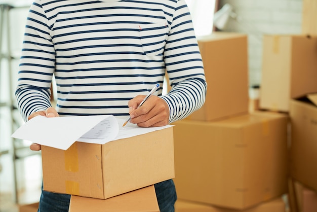 Free photo mid-section of man in striped long sleeve shirt filling out the form on the box