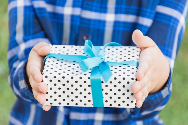 Mid section of a person holding gift box tied with blue ribbon in hand