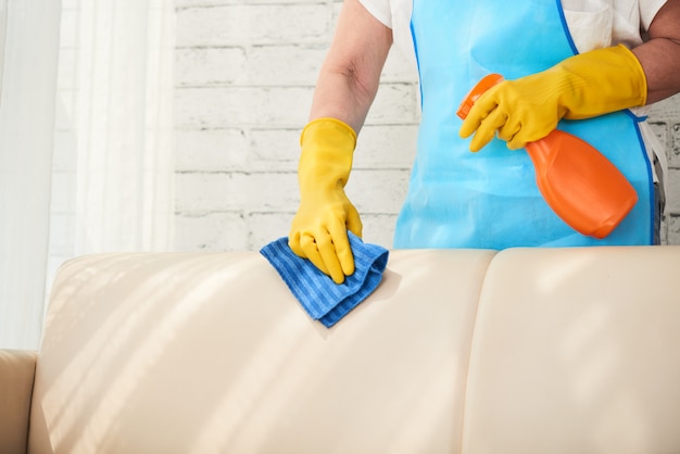 Mid section of unrecognizable housekeeper wiping leather sofa with leather polish spray