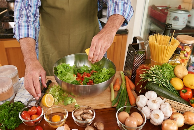 Mid section of unrecognizable man in apron adding lemon juice to the fresh salad