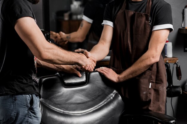 Mid section view of a barber shaking hand with male client