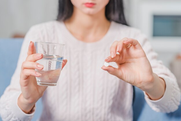 Metà di sezione di una donna che tiene compressa bianca e bicchiere d'acqua in mani