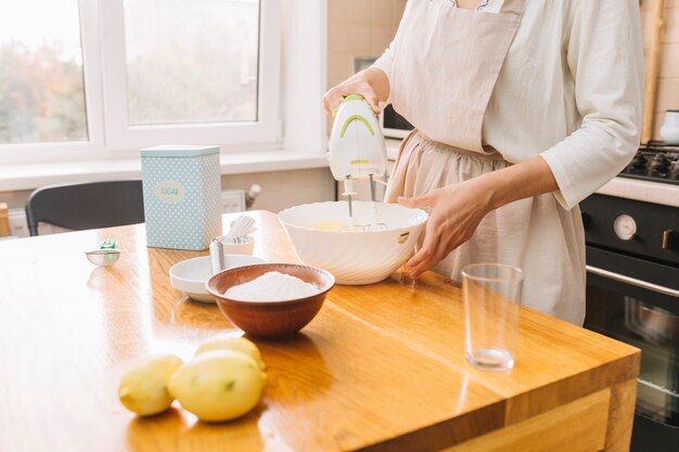 木製の机の上にパイを準備するための原料を混合する女性の中央部