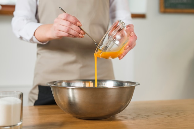 Mid section of woman pouring the egg yolk in the stainless steel bowl on wooden table
