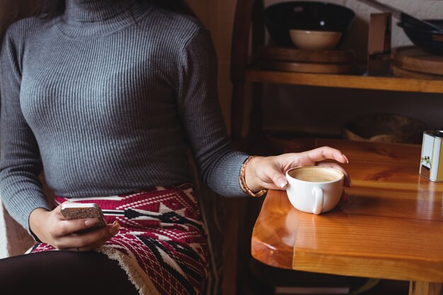 Mid section of woman using mobile phone while having a cup of coffee